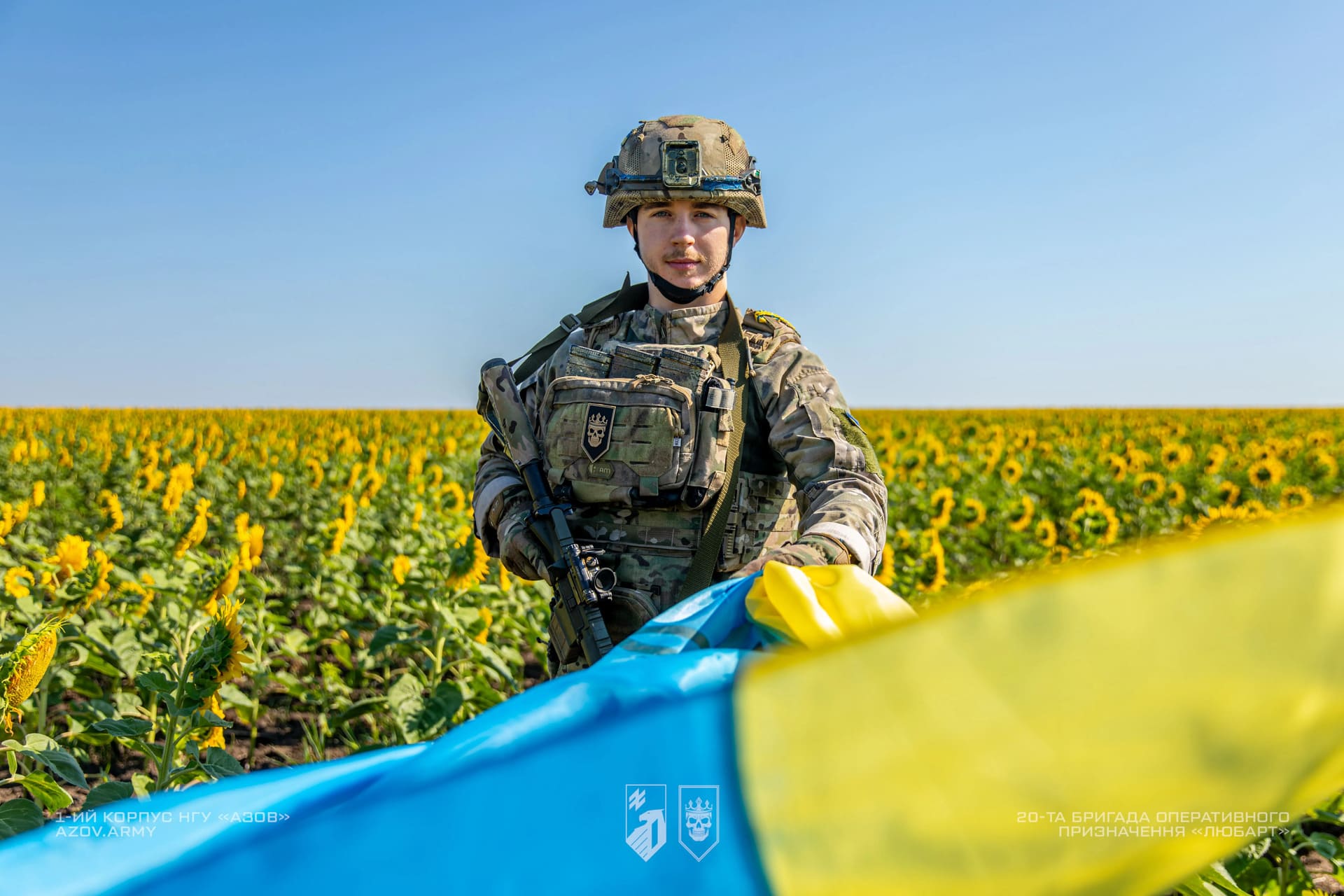 Боєць бригади Любарт тримає в руках український прапор на фоні соняшникового поля