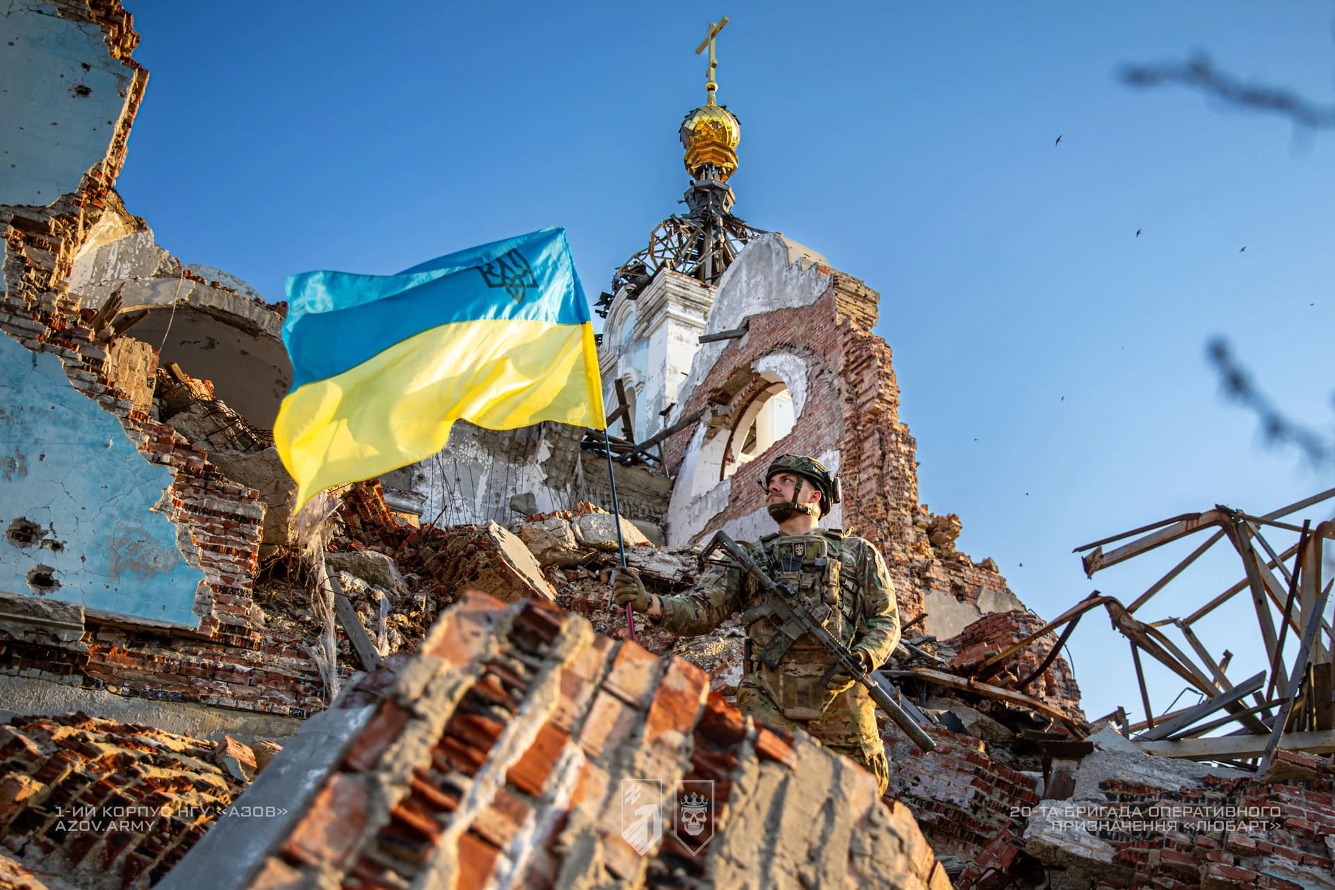 Боєць бригади Любарт тримає в руках український прапор на фоні руїн будинку