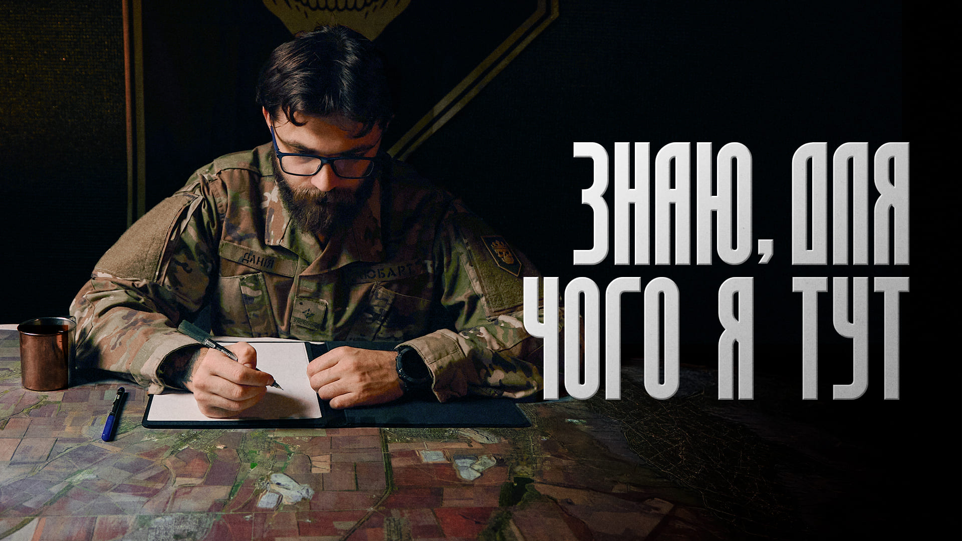 Військовослужбовець сидить за столом та дивиться на мапу, напис "Знаю, для чого я тут"